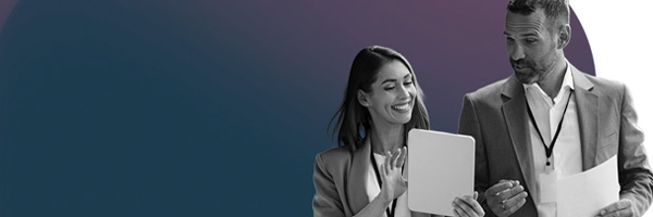 A man and woman in business attire are collaborating while examining a tablet together