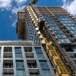 High-rise building under construction with cranes and exterior lifts.