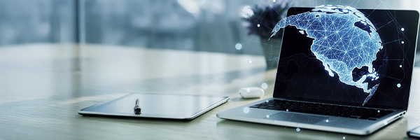 A laptop next to pen and paper at a desk.