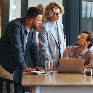 3 coworkers chatting surrounding a laptop.