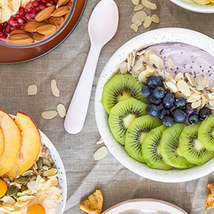 Bowl of yogurt topped with kiwi, blueberries, and nuts.