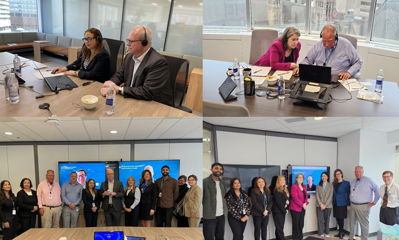 A four‑image collage shows moments from collaborative, office‑based work and team gatherings. The top left image shows three colleagues seated at a conference table wearing headsets, working on laptops during a virtual meeting, with water bottles and notes on the table. The top right image shows two colleagues seated closely at a table, leaning toward a laptop while reviewing materials together, with documents, devices, and refreshments spread across the workspace. The bottom left image shows a larger group of colleagues standing side by side in a meeting room, posing in front of wall‑mounted display screens. The bottom right image shows another group of colleagues standing together in a bright office space, arranged in a line for a group photo, with large windows and presentation screens visible.